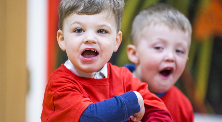 A boy with a Pyjama Drama red shirt on looks towards the camera shooting something out loud.